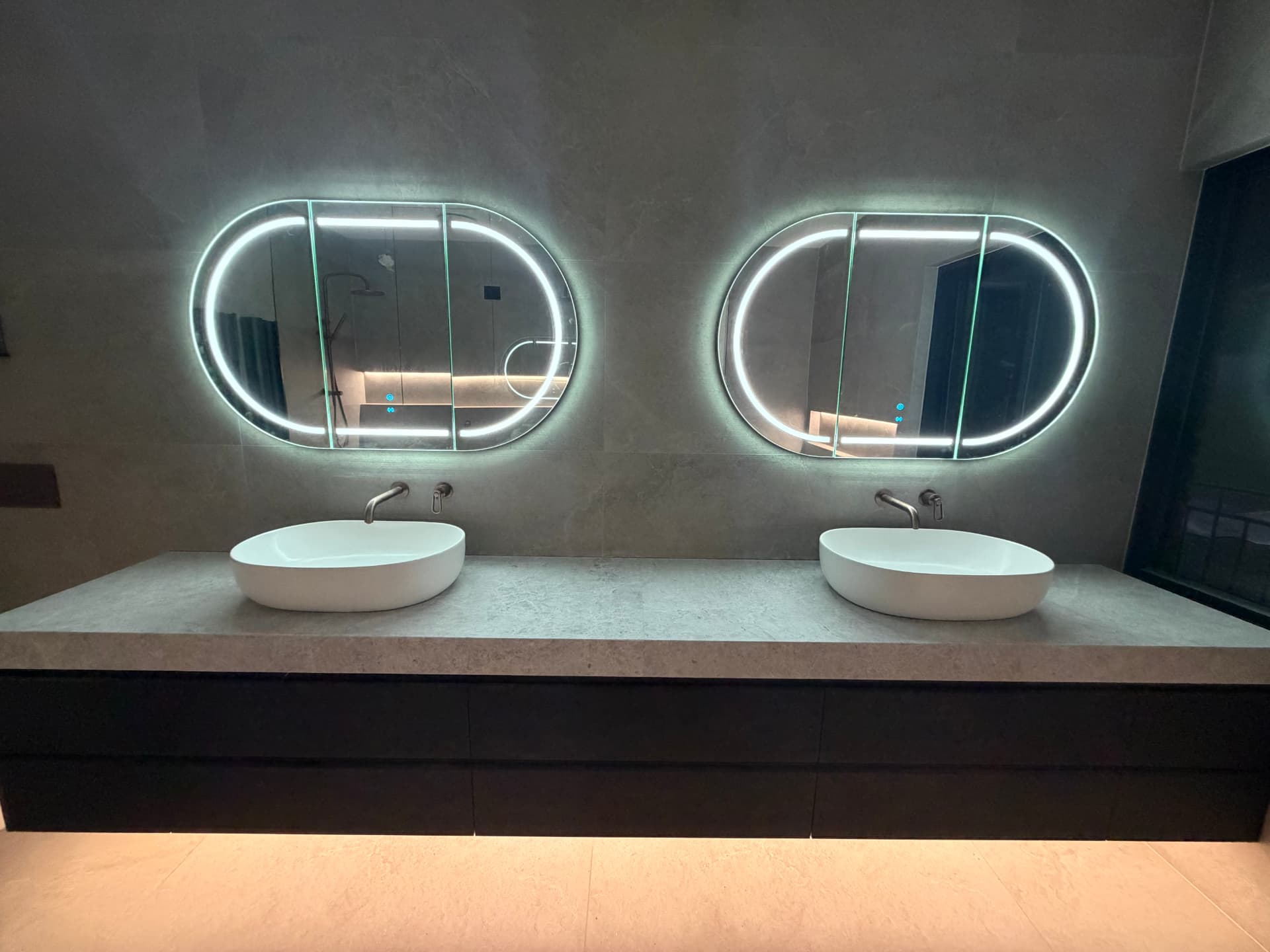 Twin backlit LED bathroom mirrors above stone vanity with under-bench lighting