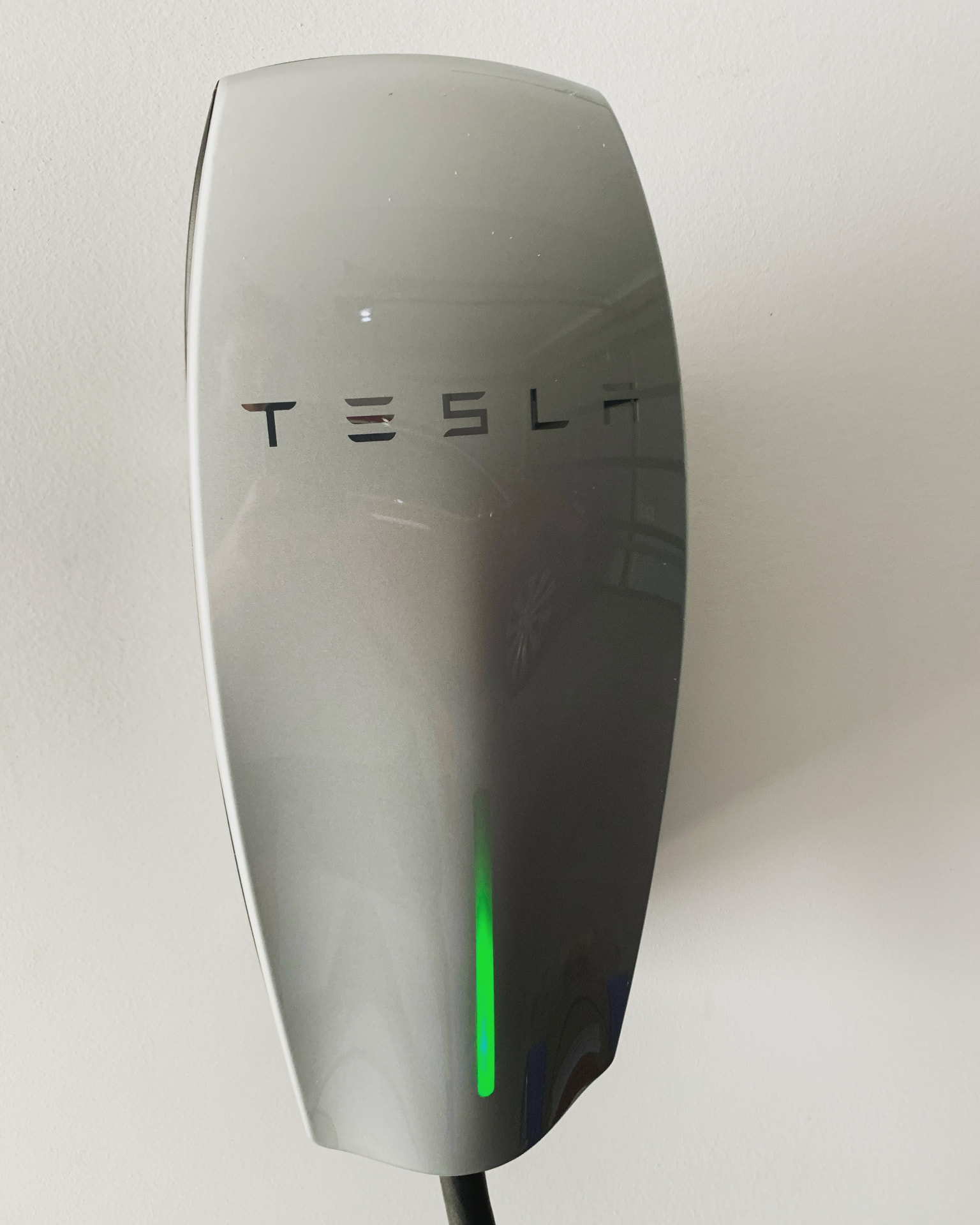 Tesla wall connector EV charger installed on a home wall, charging with a green status light
