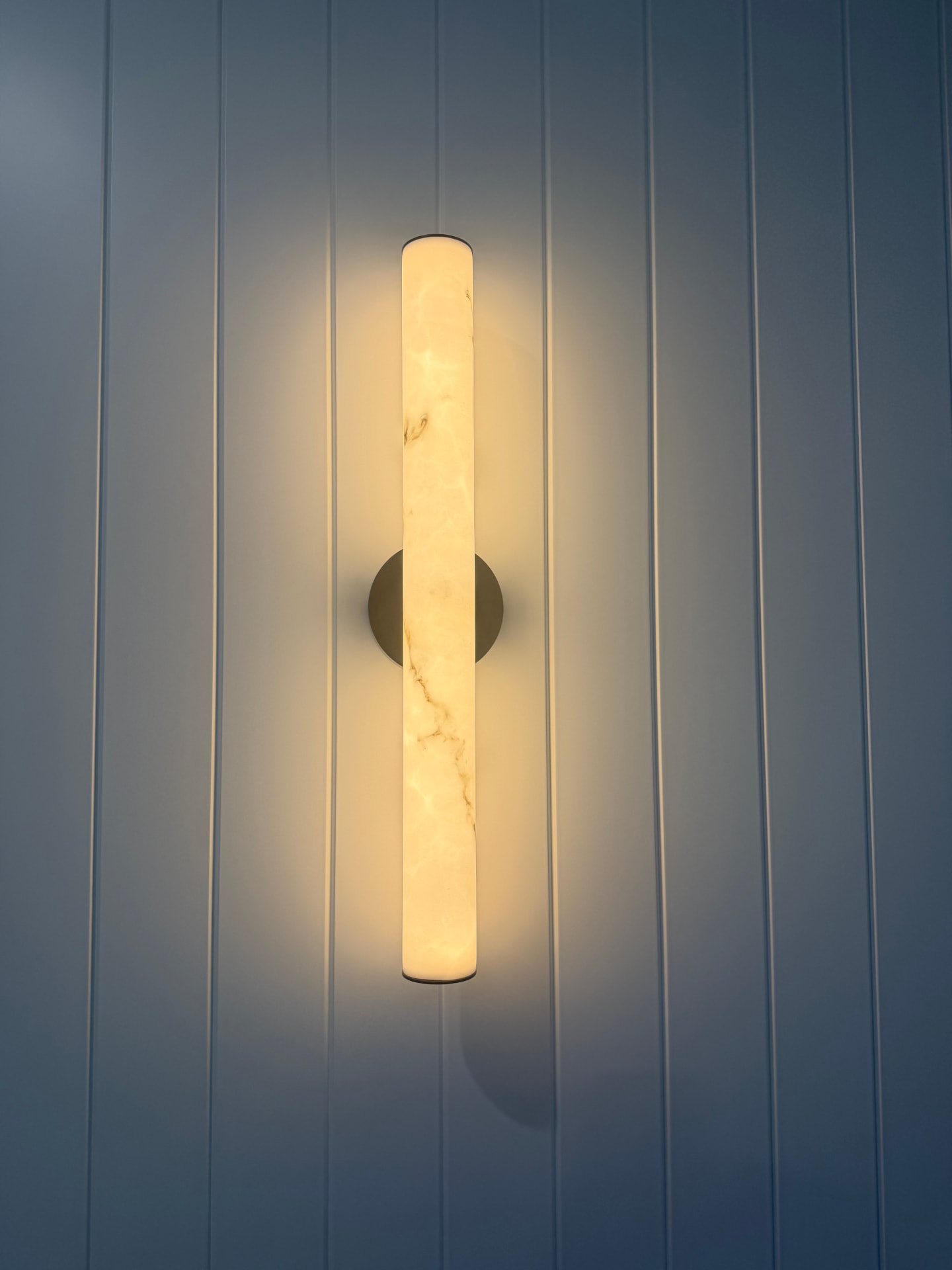 Alabaster wall sconce mounted on a blue panelled wall casting warm light